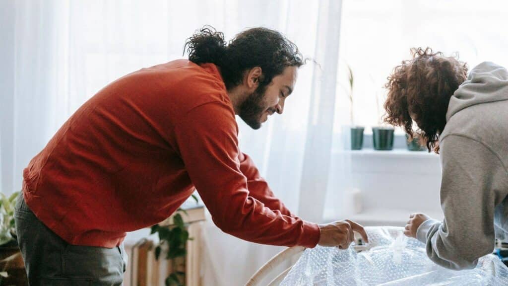 Dos personas envolviendo un mueble con plástico de burbujas antes de una mudanza